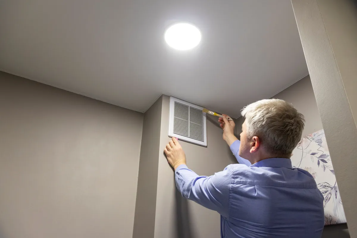 Technician cleaning a return air vent grille and duct — illustrative stock photo, not an actual St. George job site